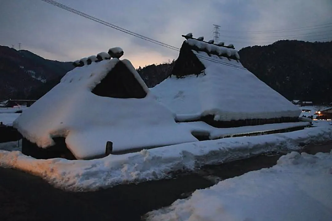 夕暮れの雪の茅葺屋根